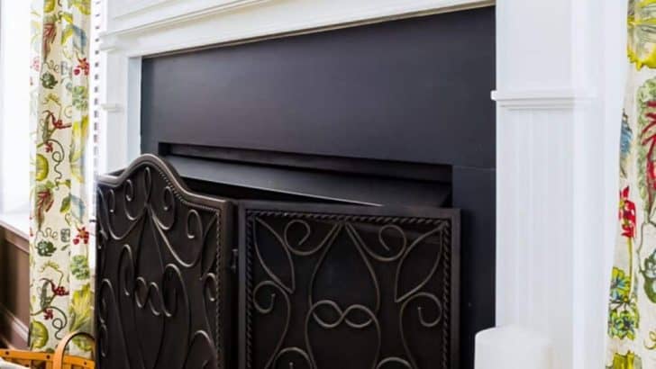 close up view of fireplace surround that has been painted with chalk paint with an iron scrollwork folding fireplace screen in front