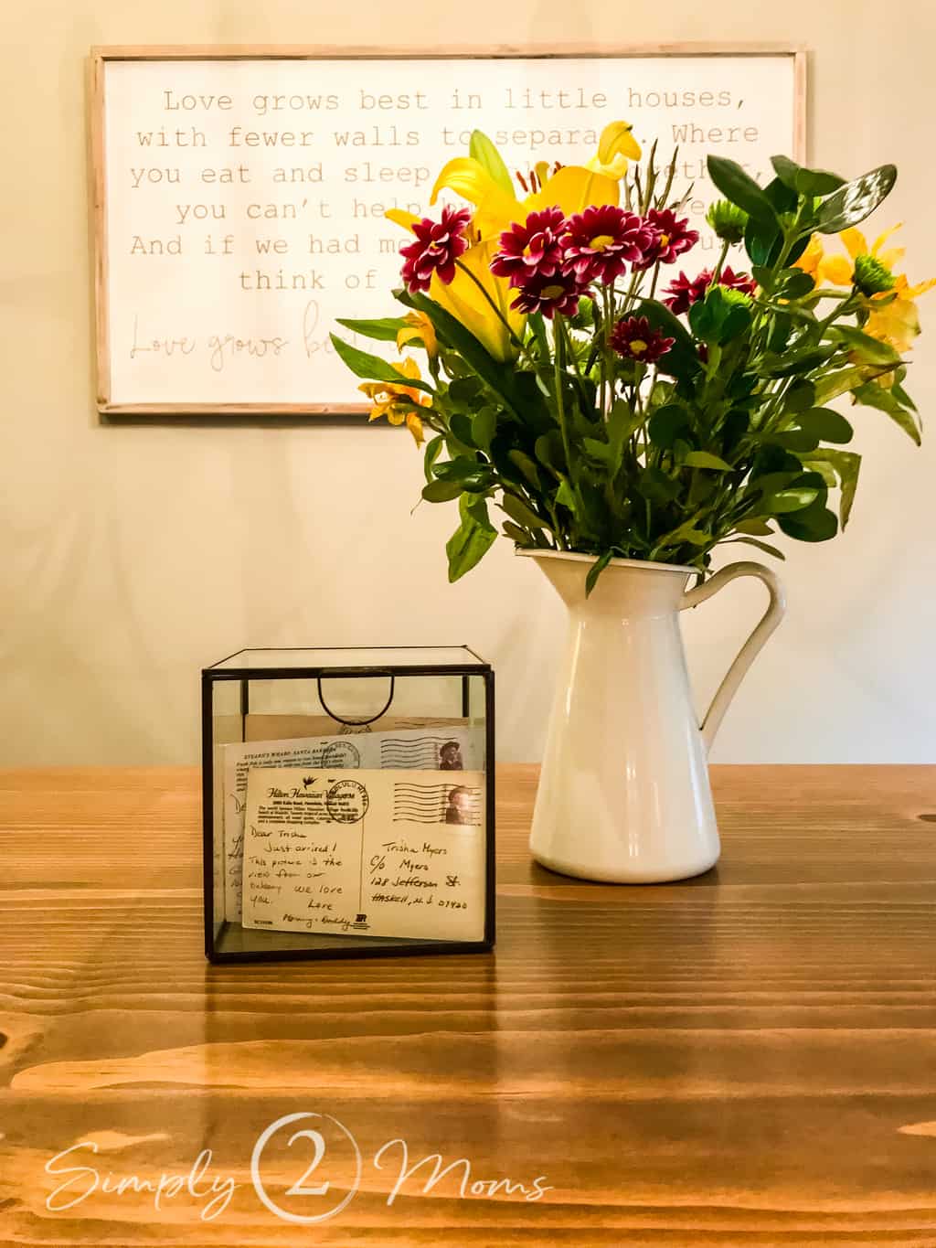 glass box filled with postcards and pitcher filled with flowers sitting on wood table