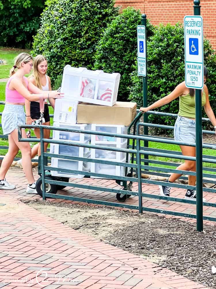 Girls pushing a wheeled flatbed cart for move in day at college.