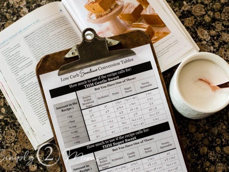 clipboard with low carb sweetener conversion table next to an open cookbook and cannister of sweetener