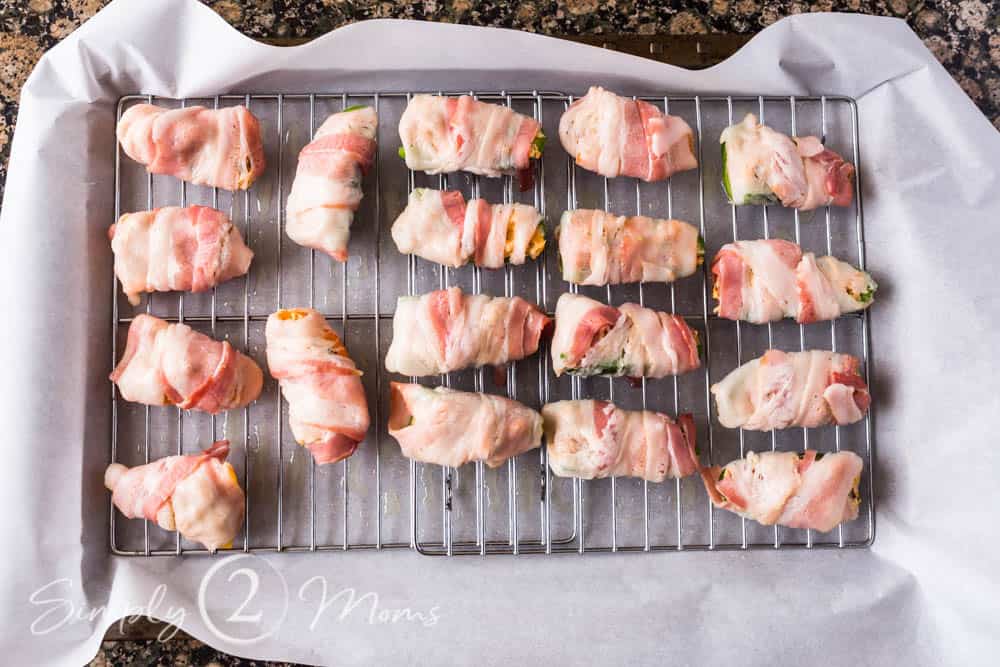 uncooked Bacon-wrapped BLT Jalapeno Poppers on wire racks in a parchment paper lined pan