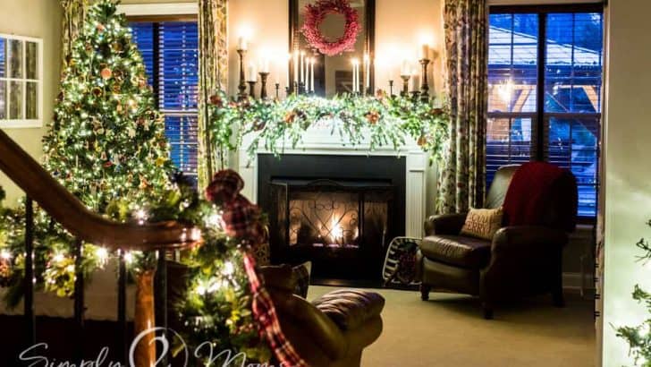 family room view with Christmas tree and lit fireplace decorated for Christmas with candle, greenery, and red berries