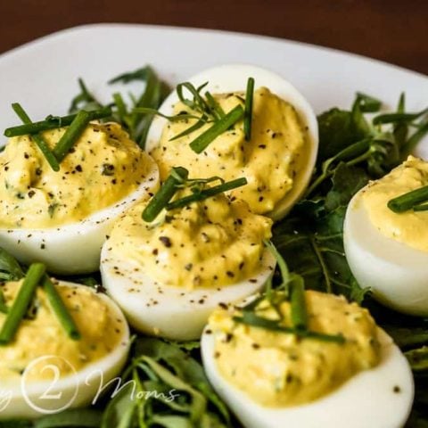 plate covered with baby lettuces and fresh taragon with deviled eggs sitting on top garnished with fresh chives