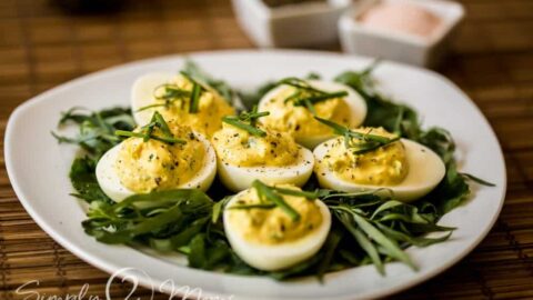 plate covered with baby lettuces and fresh taragon with deviled eggs sitting on top garnished with fresh chives