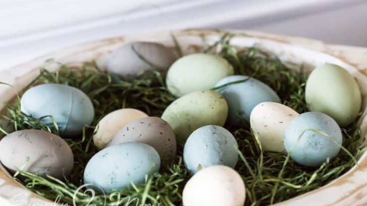 distressed white dough bowl filled with faux grass and painted plastic eggs that have been painted to look like natural eggs