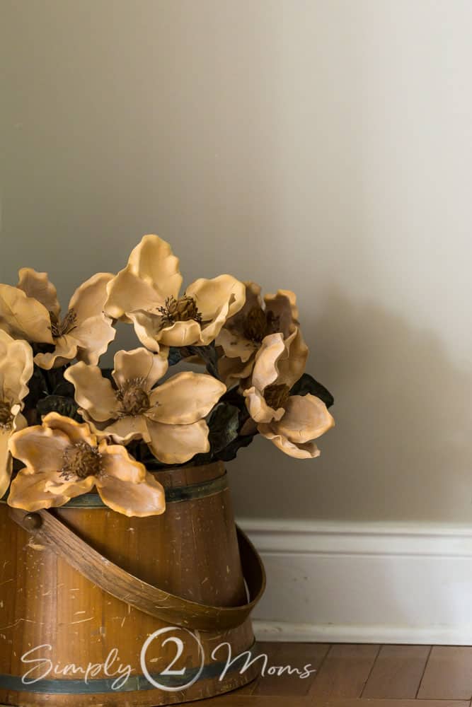 An antique wooden bucket holds a bouquet of dried faux magnolia stems