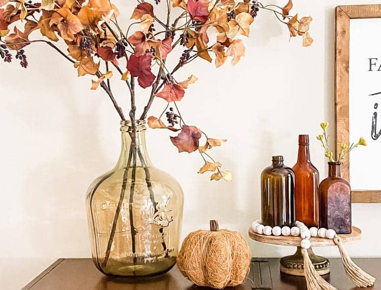display of glass vase with fall leaves pumpkin and trio of amber vintage glass bottle on top of shelf