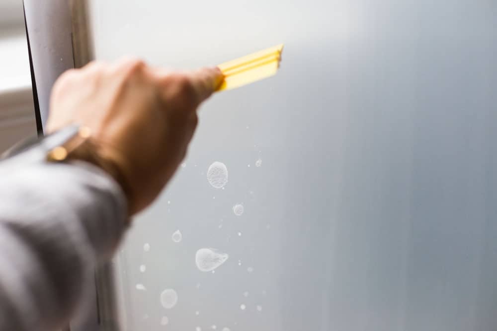hand with squeegee smoothing out air bubbles from frosted glass window film
