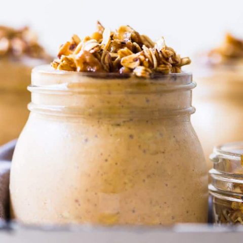 Small jars filled with pumpkin cheesecake overnight oats with a maple walnut crumble on top.