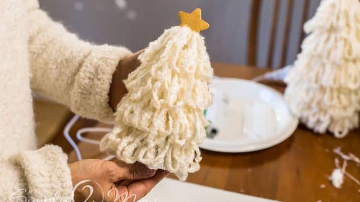 Hands holding a Christmas tree covered with long loops of fluffy cream yarn topped with a gold star