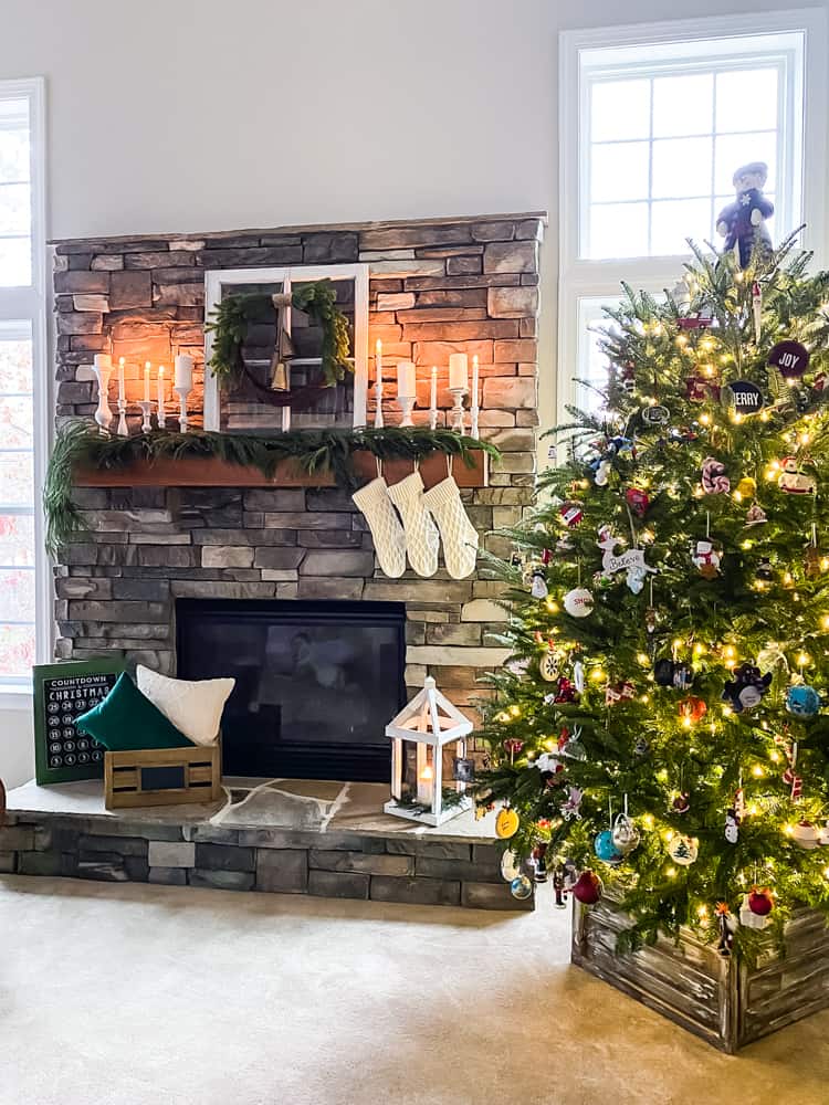 Christmas tree decorated next to stone fireplace with lit candles and garland on mantel. stockings hanging from mantel.