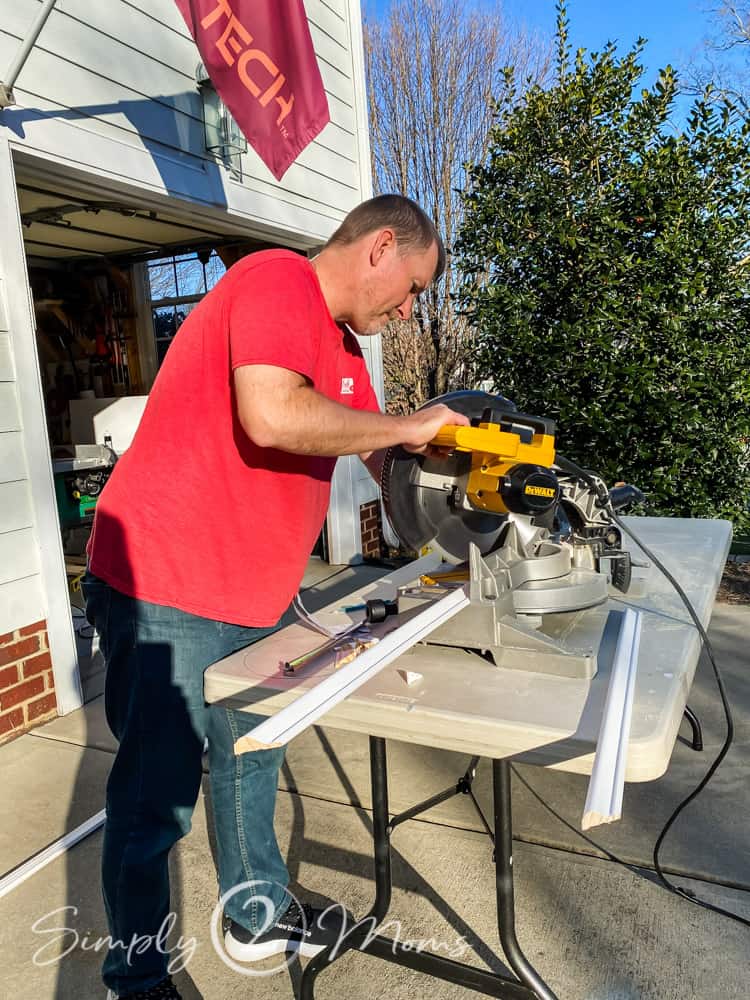 Man using a compound miter saw to cut picture moulding on a table outside
