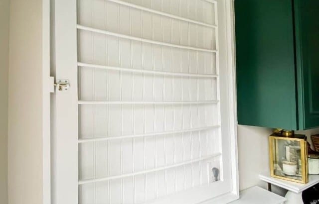 Custom DIY laundry rack with beadboard back and white painted frame hanging on the wall of a laundry room