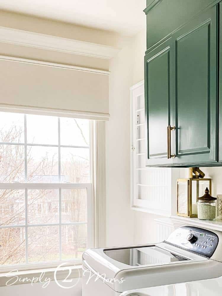 Lafayette green painted laminate cabinets with gold bar handles in a laundry room with a window.