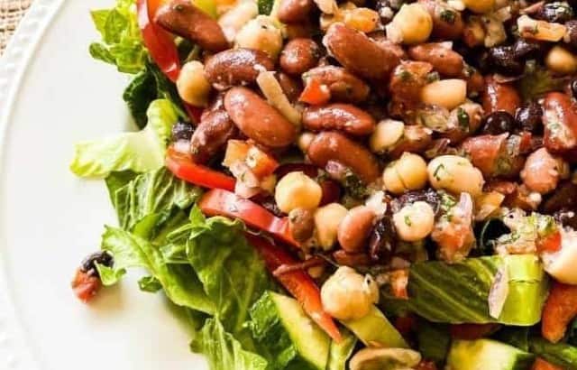 overhead view of a bed of lettuce topped with chopped cucumbers, sliced red bell peppers, chopped tomatoes, and bean salad.
