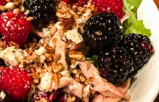 Bowl of mixed greens topped with shredded chicken, fresh raspberries and blackberries, and diced pecans