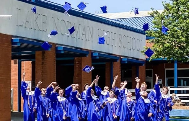group of boys in gowns throwing caps in air in front of high school for graduation