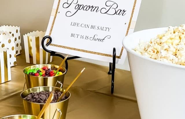 popcorn bar sign on metal easel with small buckets filled with candy in front and big tub of popcorn on side of sign