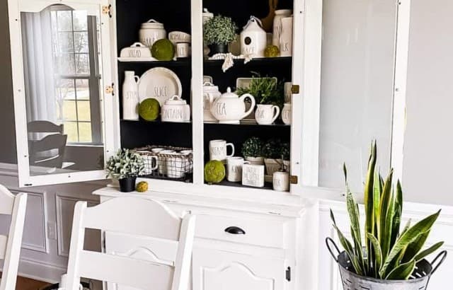 view of china cabinet over corner of dining room table with snake plant in galvanized container on top of wood stool next to china cabinet