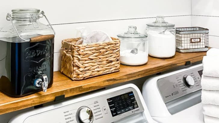 containers holding laundry products on wood shelf above washer and dryer