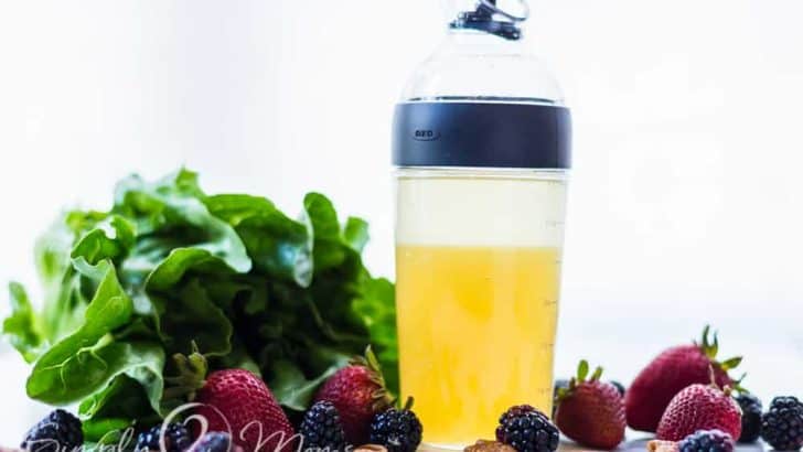 Shaker container with spout filled with Sweet low carb salad dressing surrounded by lettuce, fresh strawberries, blackberries, and walnuts