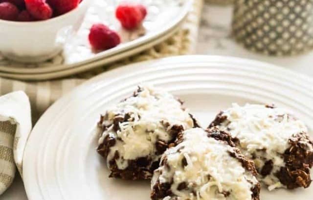 Three Chocolatey Peanut Butter Banana Breakfast cookies styled on a plate with a bowl of raspberries in the background with a sugar bowl and cream pitcher.