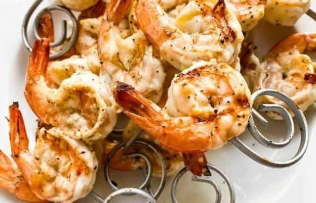 Cooked shrimp on circular kebab skewers with a spiral end stacked on a plate
