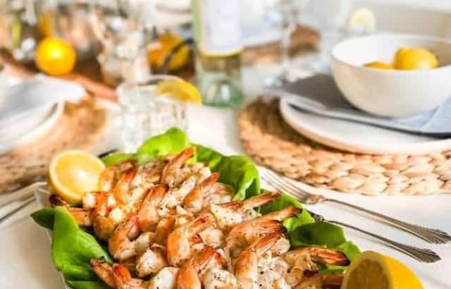 Table set for dinner with white dishes and lemons with a platter of grilled lemon pepper shrimp on a bed of lettuce