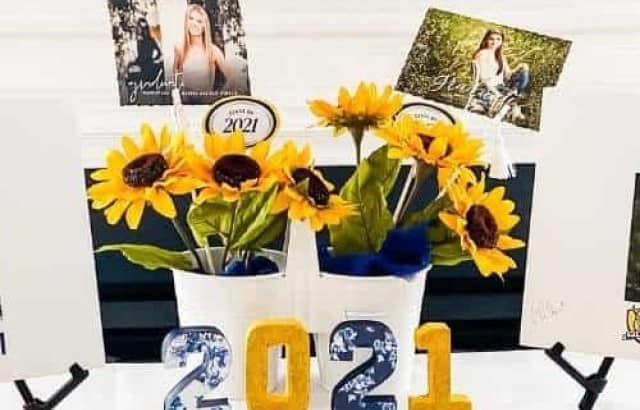 Table with a display of high school diplomas, foam board signs with pictures of the graduates, a centerpiece of sunflowers and the graduation announcements at a graduation party for twin sisters.