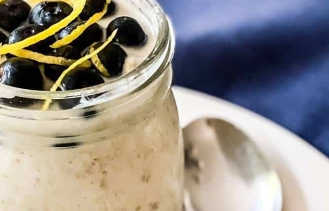 A single-serving jar of lemon blueberry overnight oats garnished with lemon zest with a spoon sitting next to it.
