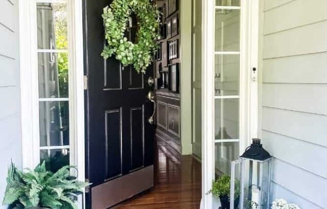 Front entry with lanterns and black front door with a transom and full side light windows with a large succulent wreath.