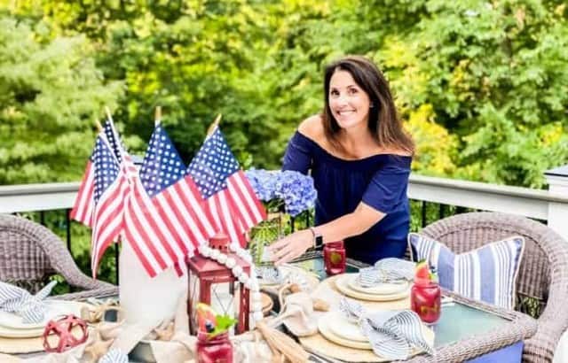 woman placing vase of cut hydrangea on table set for patriotic dinner party
