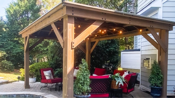 Gazebo with overhead ceiling fans, string lights sits on a paver patio next to a pool.