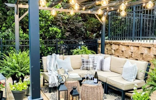 metal pergola on patio outside with furniture and throw pillows, area rug, tables, lanterns and plants around area