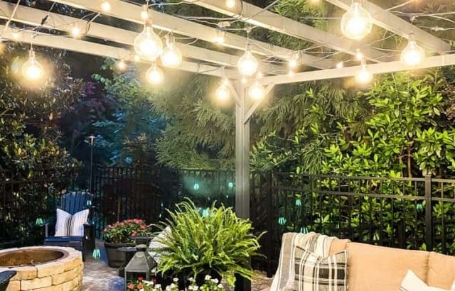 nighttime view of metal pergola with string lights lit up on patio above seating area
