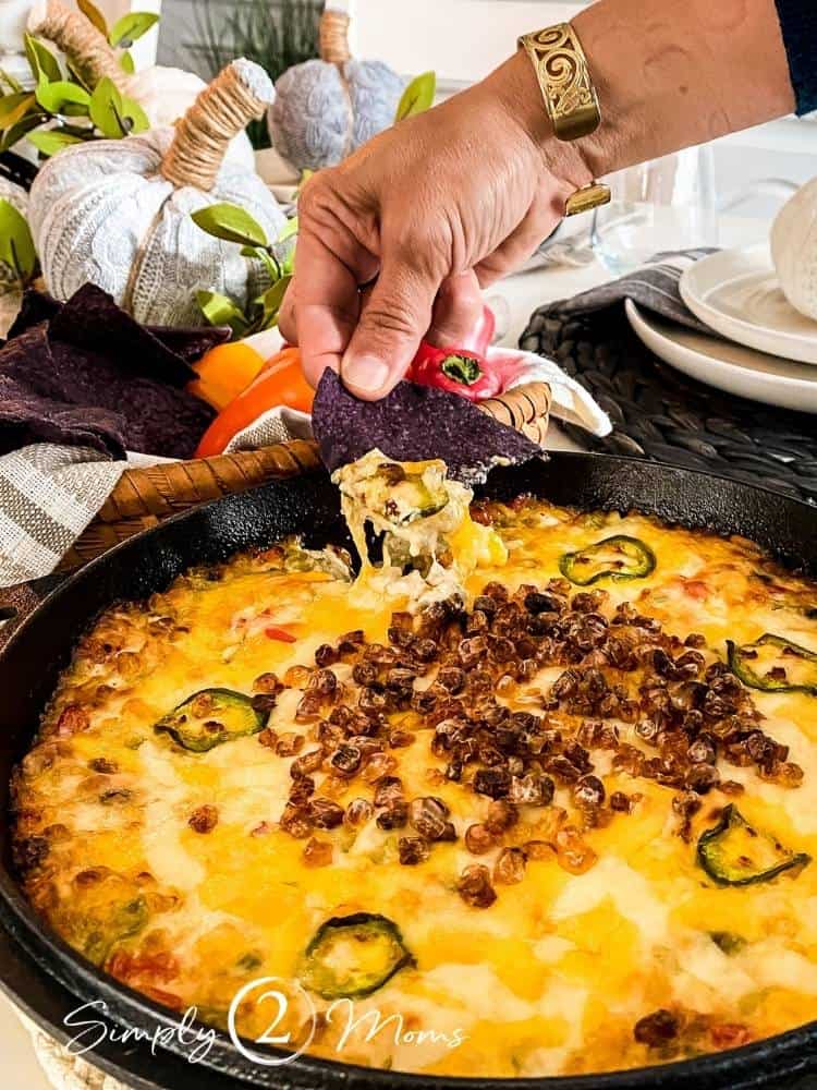 Hand holding a blue corn tortilla chip dipped into Hot Roasted Corn Dip