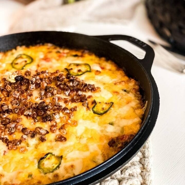 Cast iron skillet of Hot Roasted Corn Dip on a table with a cream knit trivet.