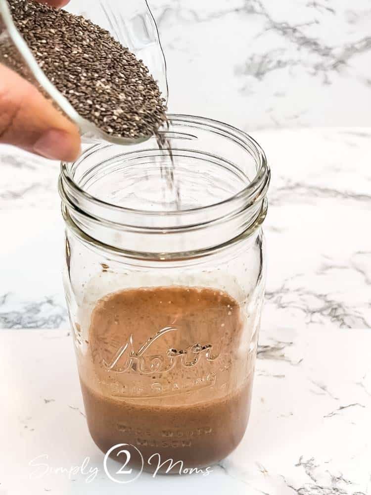 Adding chia seeds to large mason jar with chocolate almond milk