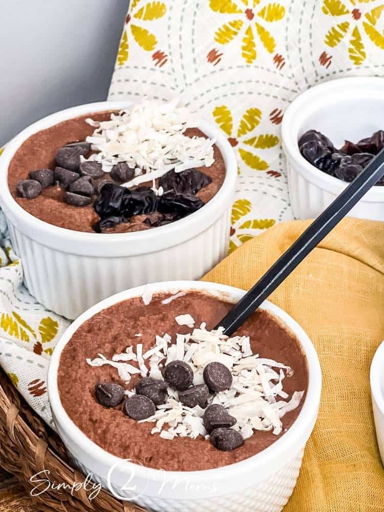 Two ramekins of Mexican Chocolate Chia Pudding topped with coconut flakes and chocolate chips