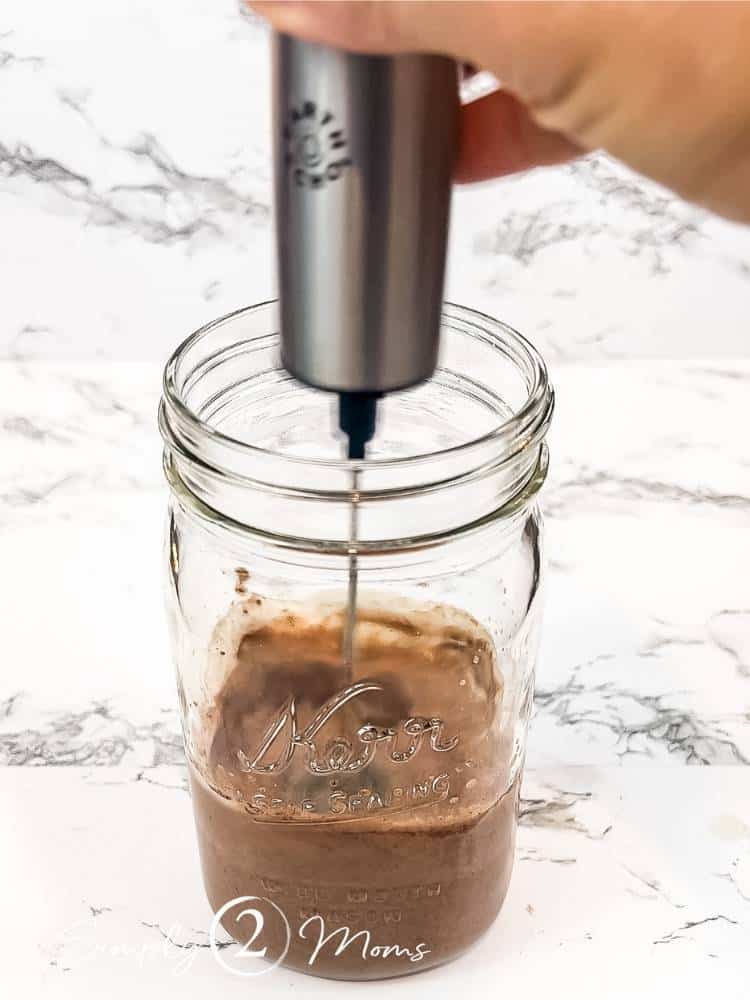 Hand holding a frother to mix chocolate chia pudding in a large mason jar