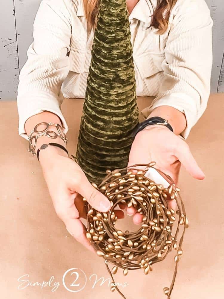 Woman holding garland covered in tiny gold beads in front of a DIY yarn tree