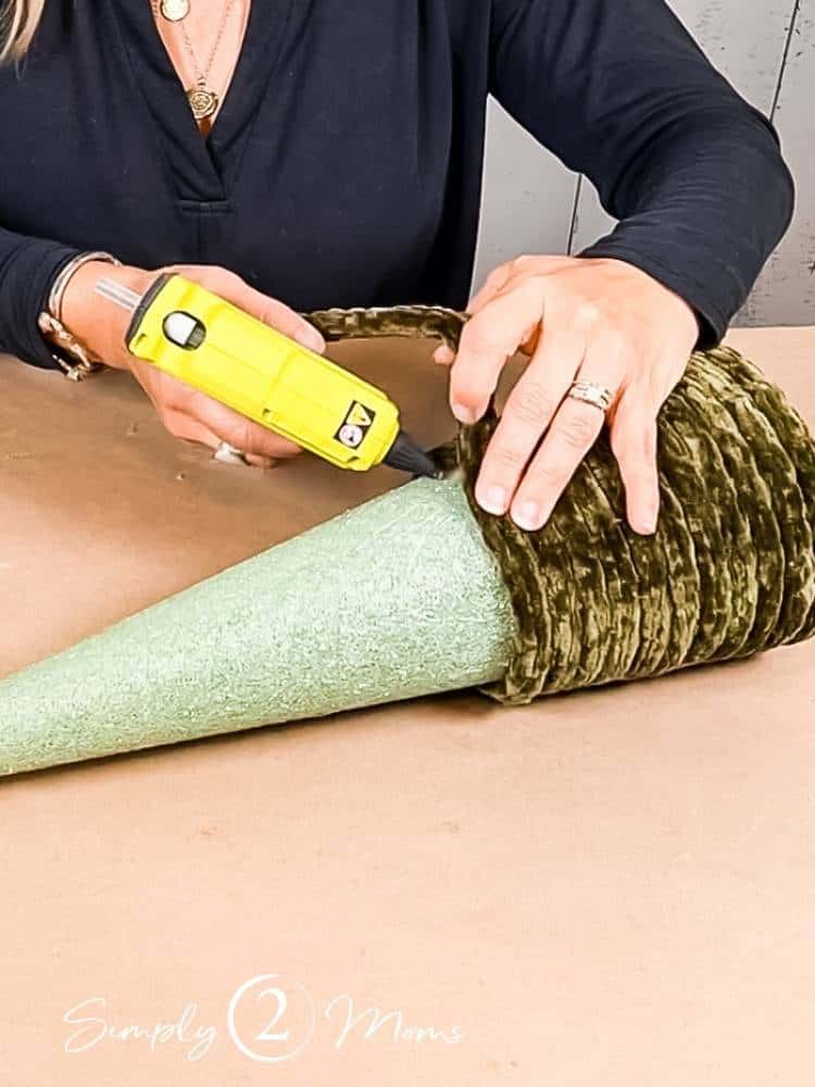 Woman using Ryobi compact glue gun to attach jumbo velvet yarn to a foam tree form