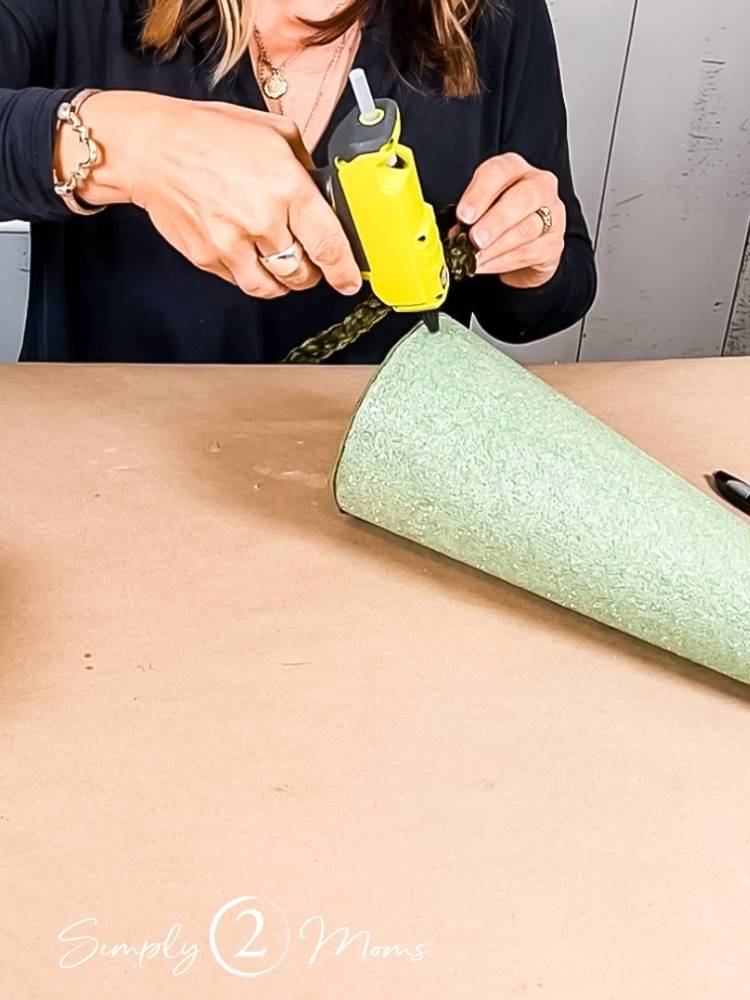 Woman using Ryobi compact glue gun to attach jumbo velvet yarn to the bottom of a foam tree form
