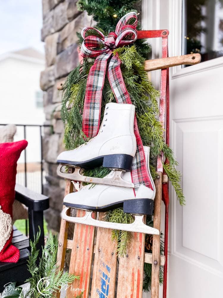 DIY plaid wired ribbon bow hanging with greenery from vintage sled with old ice skates