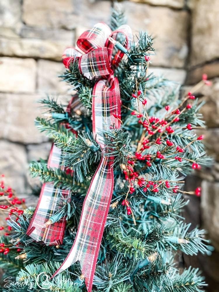 plaid holiday bow on top of small Christmas tree on porch