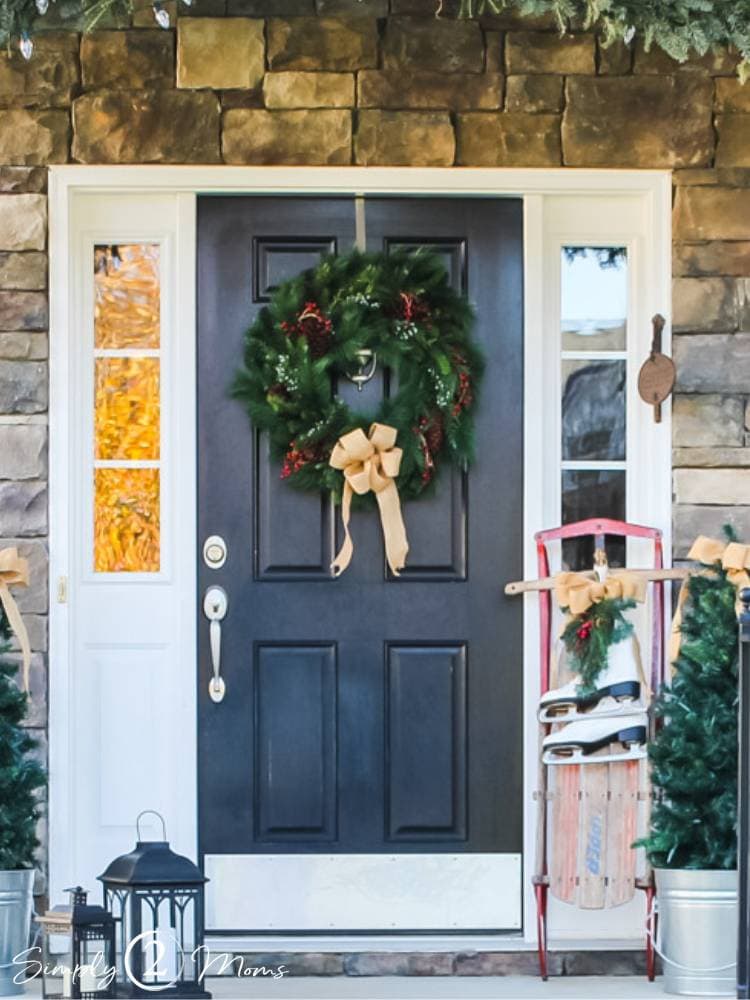 front door with Christmas wreath and burlap bow hung vintage sled and skates leaning on door