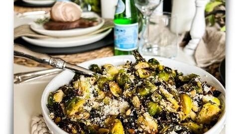 Bowl of crispy air fryer Parmesan Garlic Brussels Sprouts sprinkled with freshly grated Parmesan cheese on a dinner table.