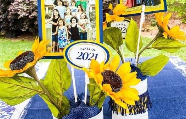 Graduation party centerpieces made from an upcycled can with ribbon, sunflowers, and photos of the graduates on a table.