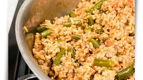Stainless steel skillet with a simple healthy recipe using ground turkey, brown rice, caulirice, green beans, and tomatoes.