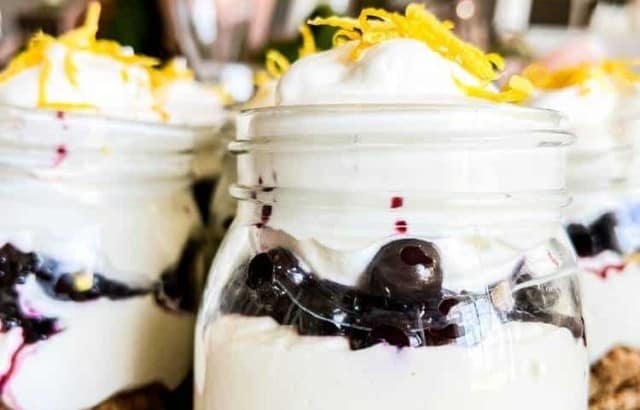 Small jars filled with low carb keto Blueberry Lemon Delight Parfaits on a table garnished with lemon zest